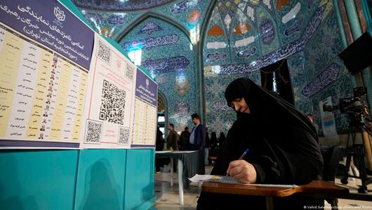 A woman holds a pen in her hand as she looks at a ballot paper at a polling station in Iran
