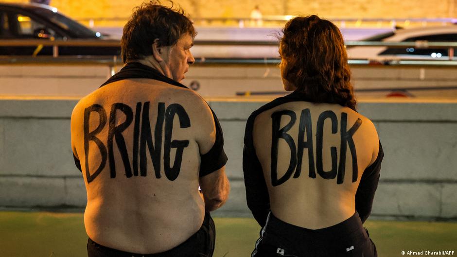 A man and a woman with the English words "BRING BACK" painted on their bare backs sit during a demonstration calling for the release of hostages held by Hamas since 7 October