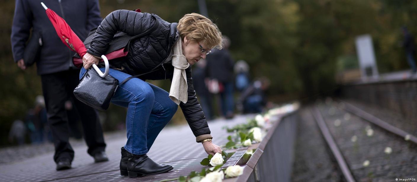 Eine Frau legt weiße Rosen nieder am Mahnmal Gleis 13 am Berliner Bahnhof Grunewald