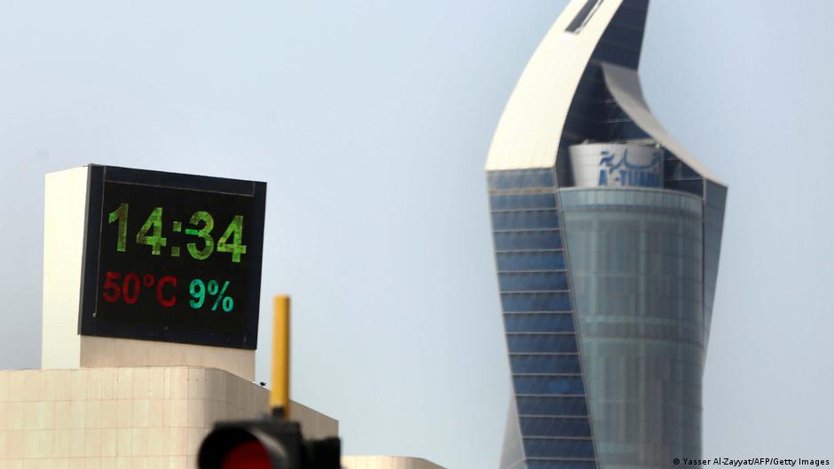 Das Temperaturmessgerät in Kuwait City zeigt eine Außentemperatur von 50° Celsius an. Im Hintergrund ist ein moderner Wolkenkratzer zu sehen