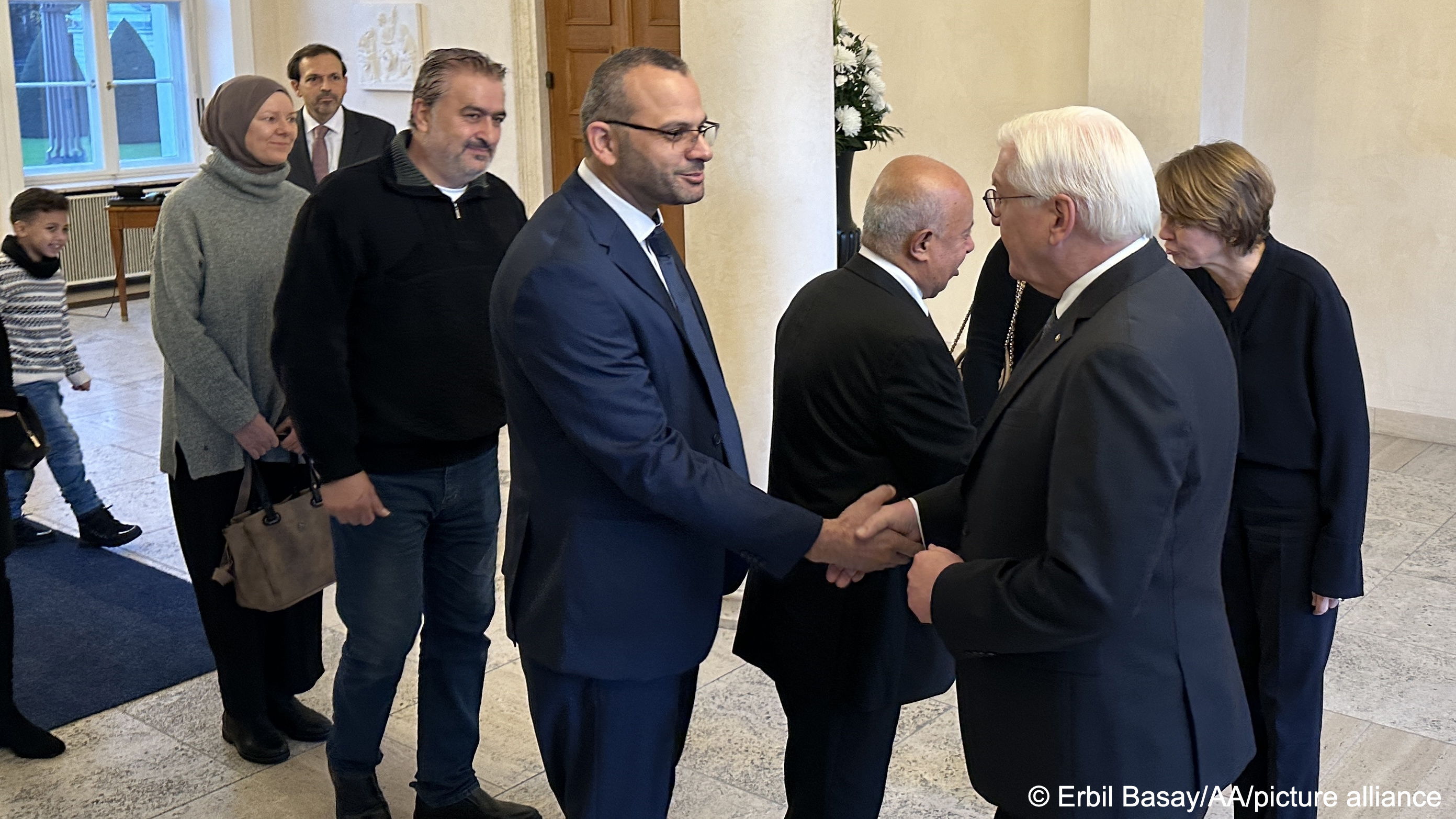 Ahmed Abunada in suit and glasses shakes hands with German President Frank-Walter Steinmeier (right), amidst a group of people waiting to be greeted