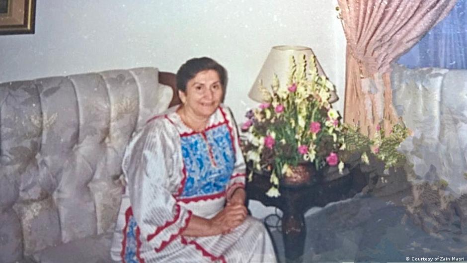 Elderly lady sits on a couch wearing a traditional Palestinian dress with tatreez embroidery