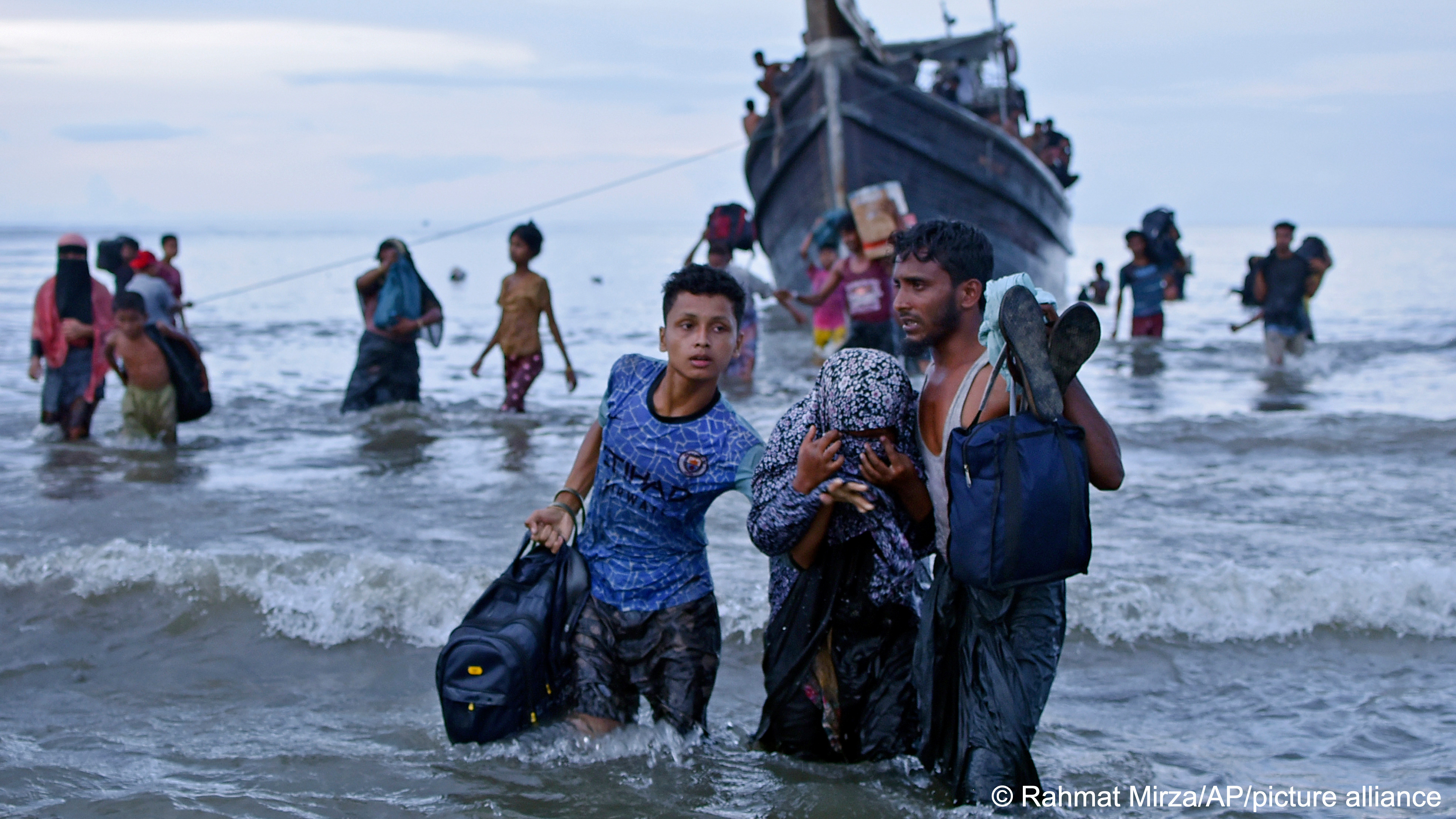 Refugees carry their belongings as they make their way ashore through the waves from a boat on the coast of Aceh, Indonesia, 16 November 2023