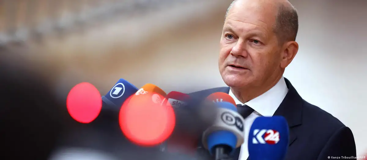 Headshot of German Chancellor Olaf Scholz as he speaks into a bundle of colourful press microphones