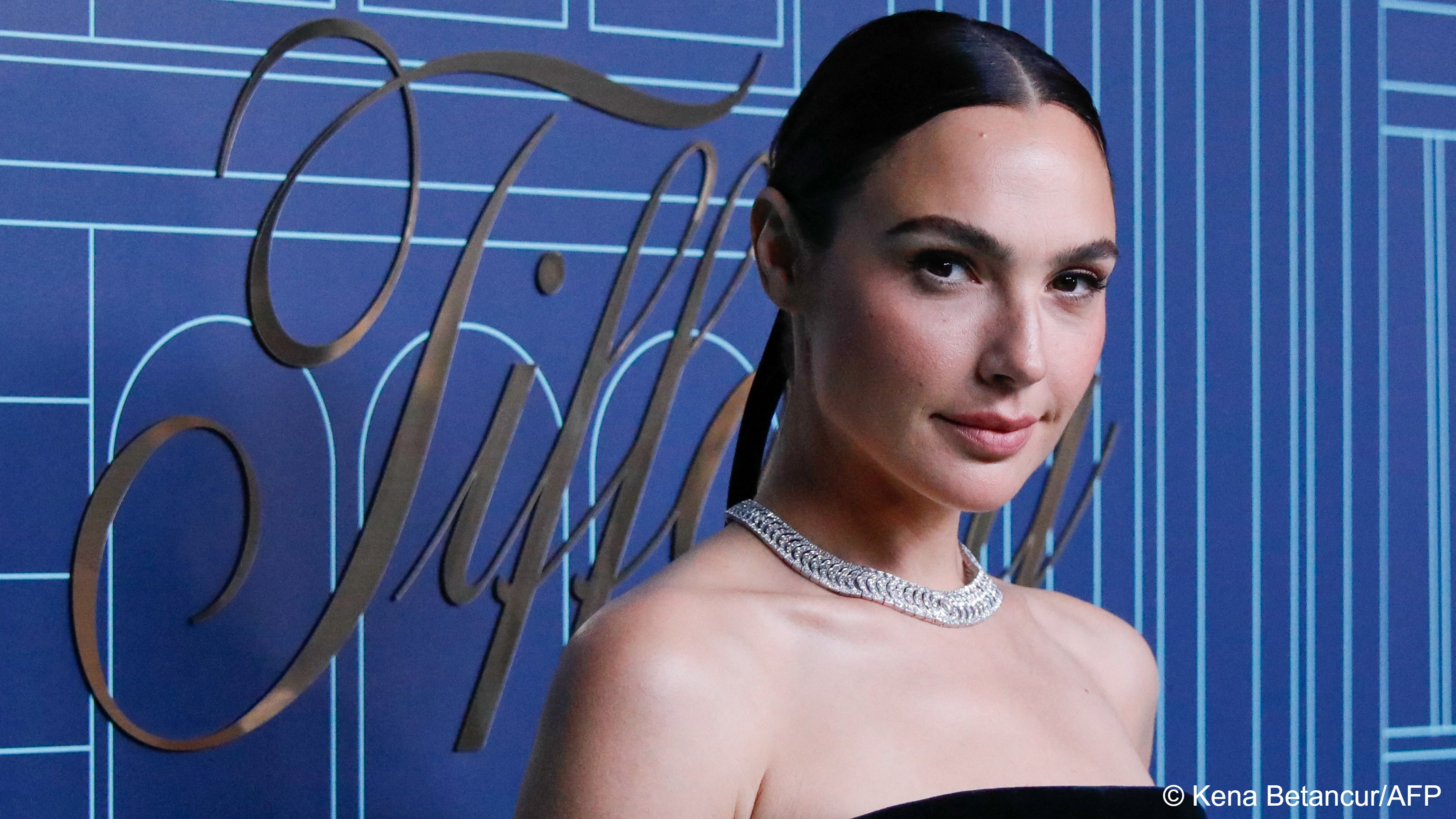 Portrait of Israeli actress Gal Gadot in evening dress, standing against a blue patterned background