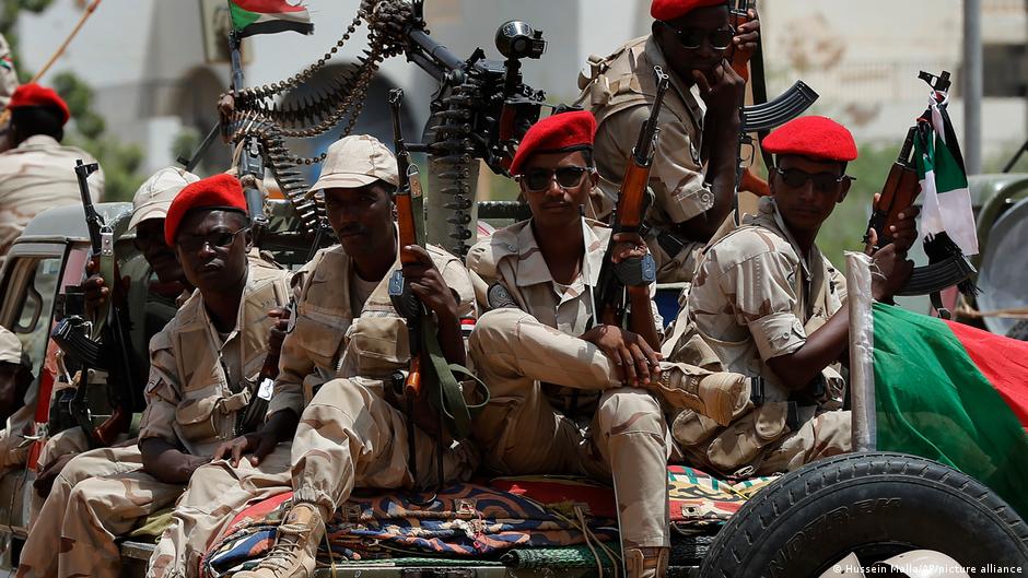 Sudanese soldiers from the Rapid Support Forces unit sit on the back of a truck wearing red berets, army fatigues and carrying automatic weapons