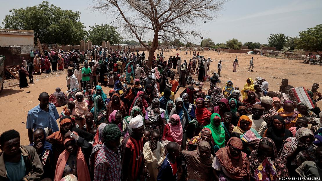 A large crowd of Sudanese refugees stands in the sun waiting to be transferred to Chad