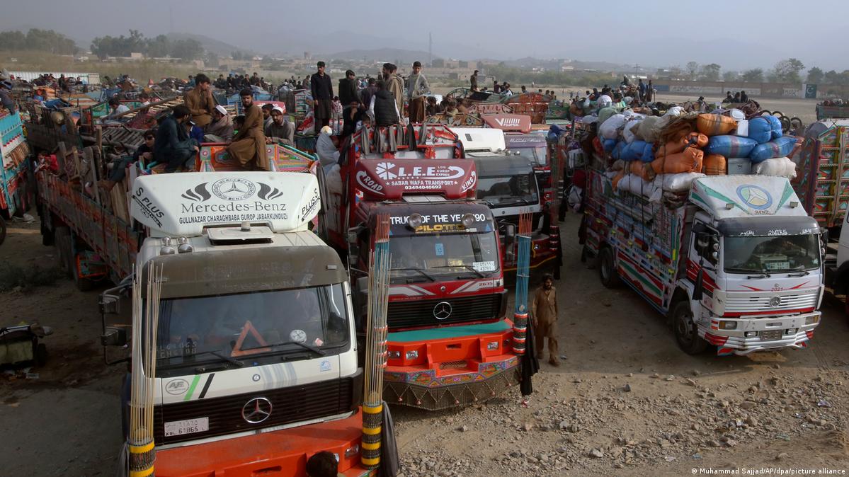 Fully packed trucks gathered at the Afghan border. People stand and sit on top of the cargo on the trucks