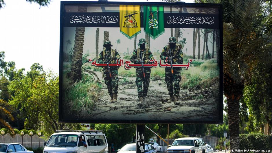 A propaganda billboard for the pro-Iran Hezbollah Brigades militia hanging over Palestine Street in the centre of the Iraqi capital Baghdad, depicting three of their masked fighters walking along a road between palm trees