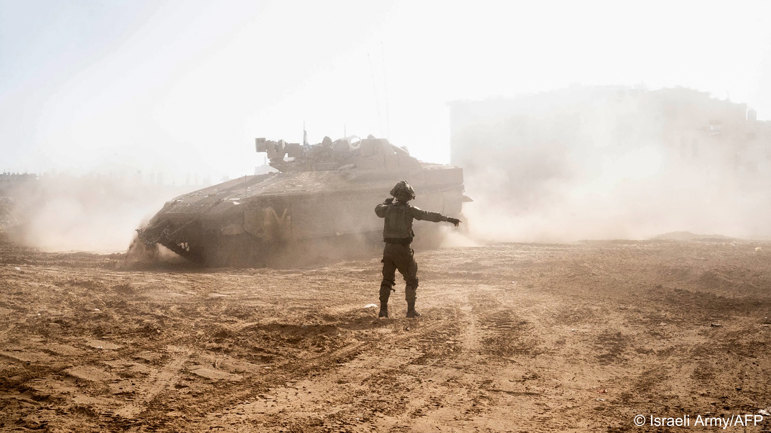 Israeli soldier stands in front of an Israeli tank in Gaza and signals with his right arm