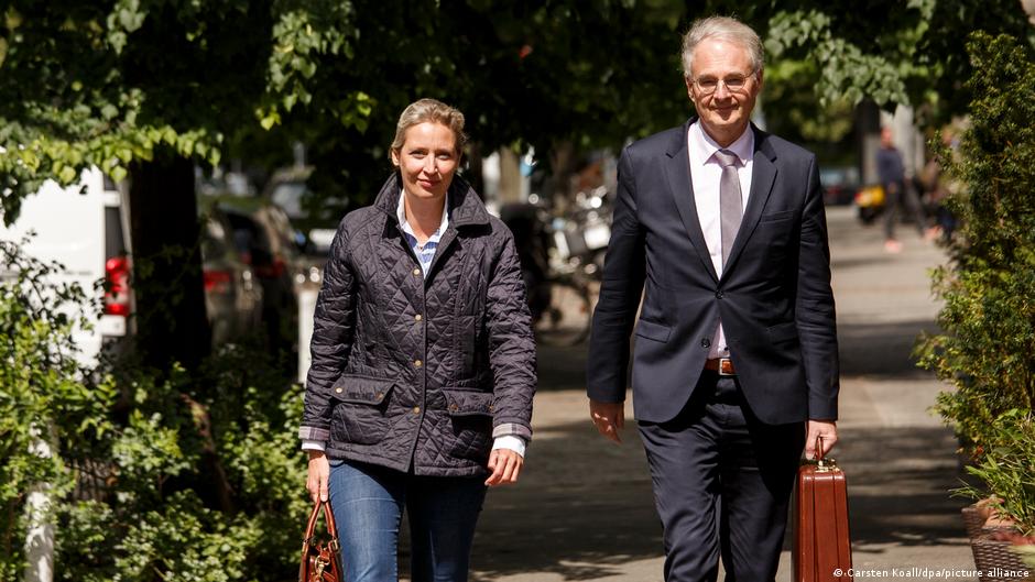 AfD co-leader Alice Weidel and her advisor Roland Hartwig walk towards the camera along a tree-lined street