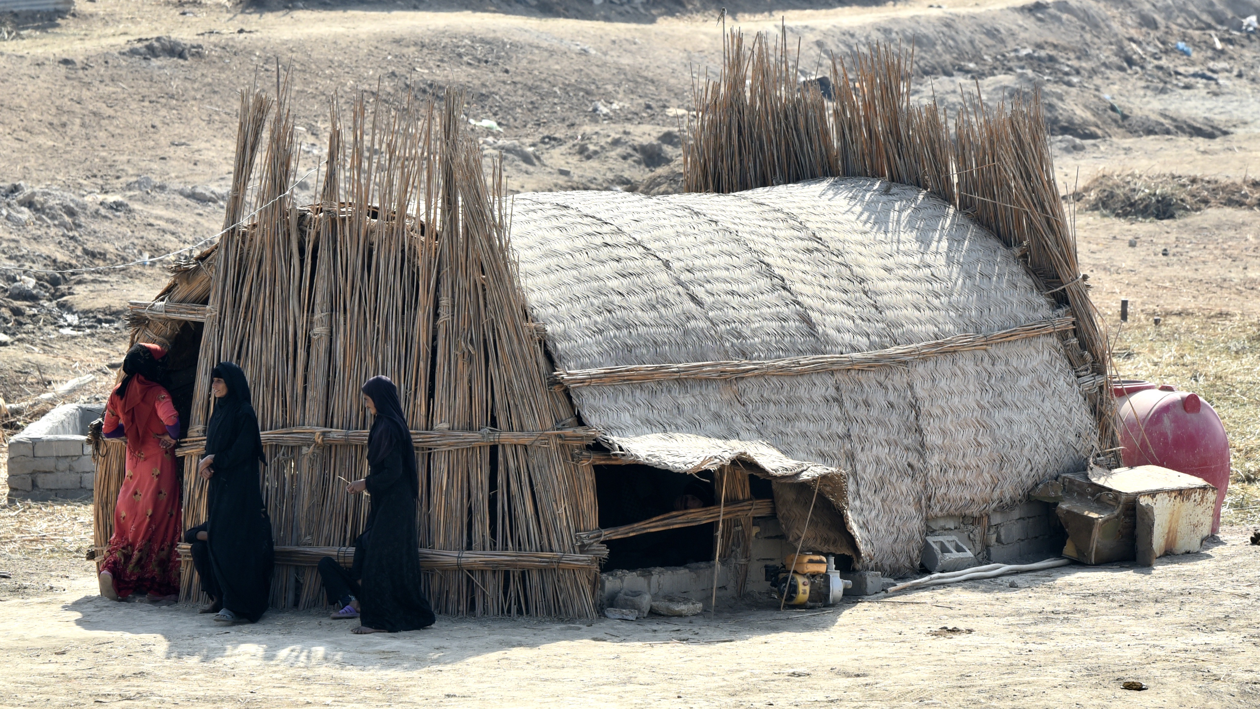 Marsh Arab women stand in the shade in front a traditional structure in Chibayish, Iraq