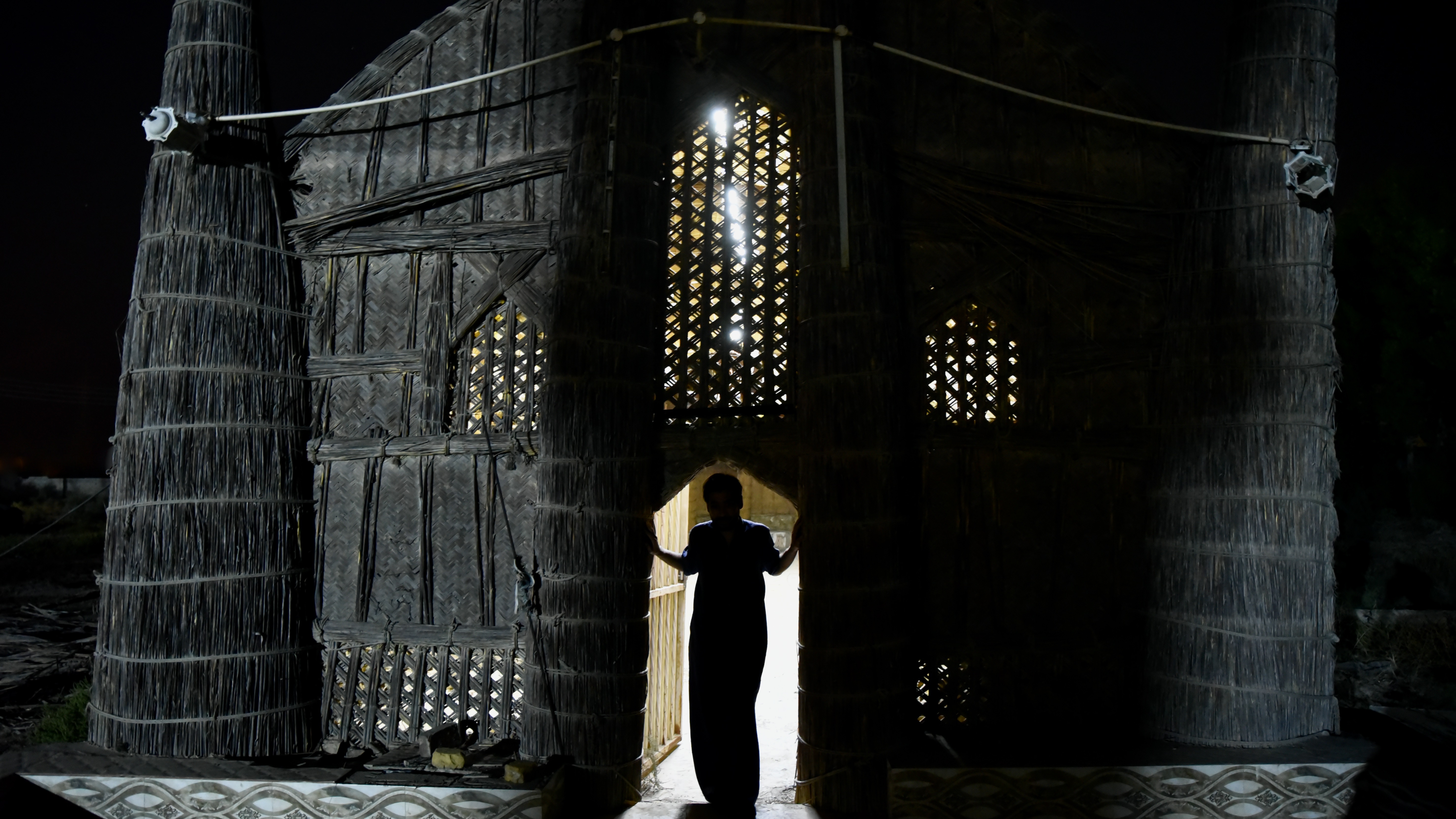 A figure silhouetted in the doorway of a traditional Marsh Arab mudhif