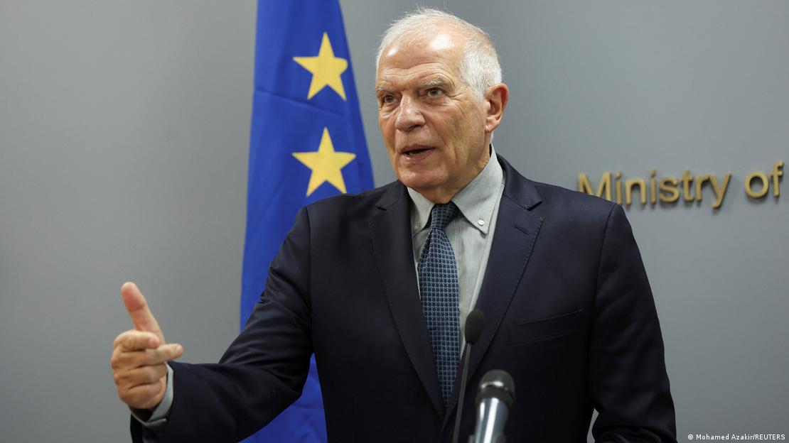 EU foreign policy chief Josep Borrell gestures as he speaks into a microphone in front of an EU flag 