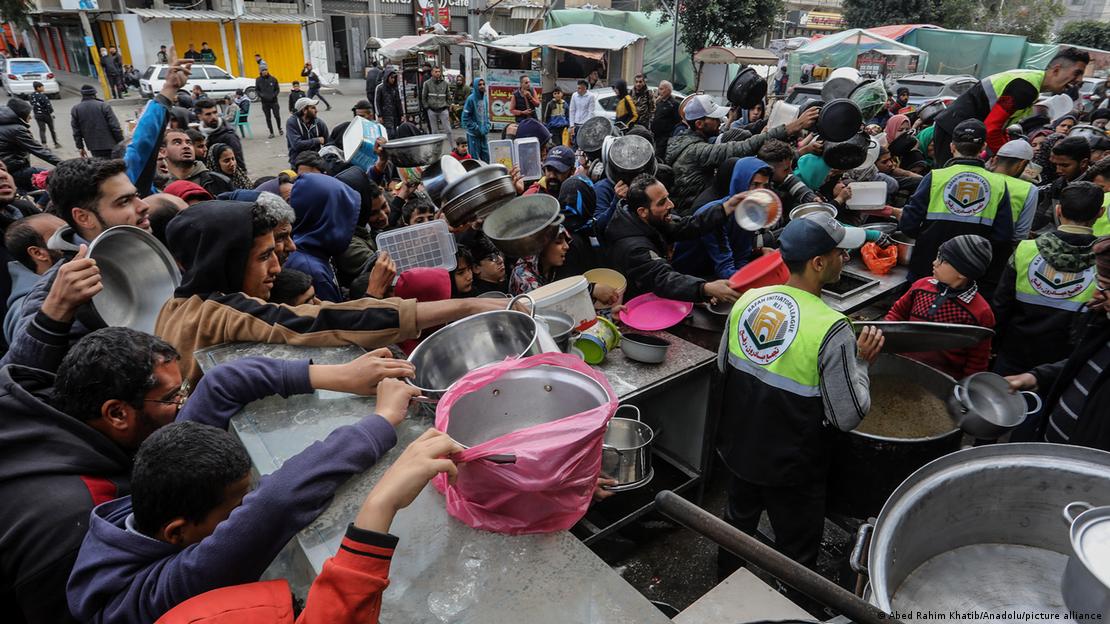 A crowd of people hold out pots, bowls and containers as they wait to receive food from a charity kitchen in Gaza