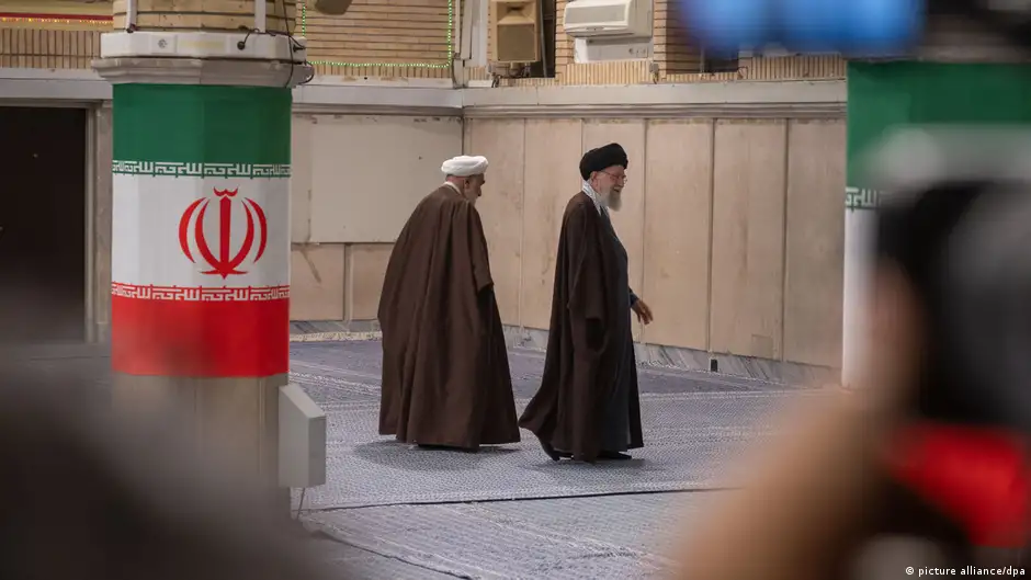 Ayatollah Khamenei (right) and another man walk between two pillars adorned with the flag of Iran