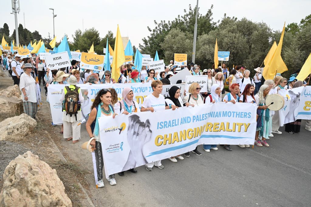 Women with yellow and turquoise scarves and flags and holding banners and placards march together down a road