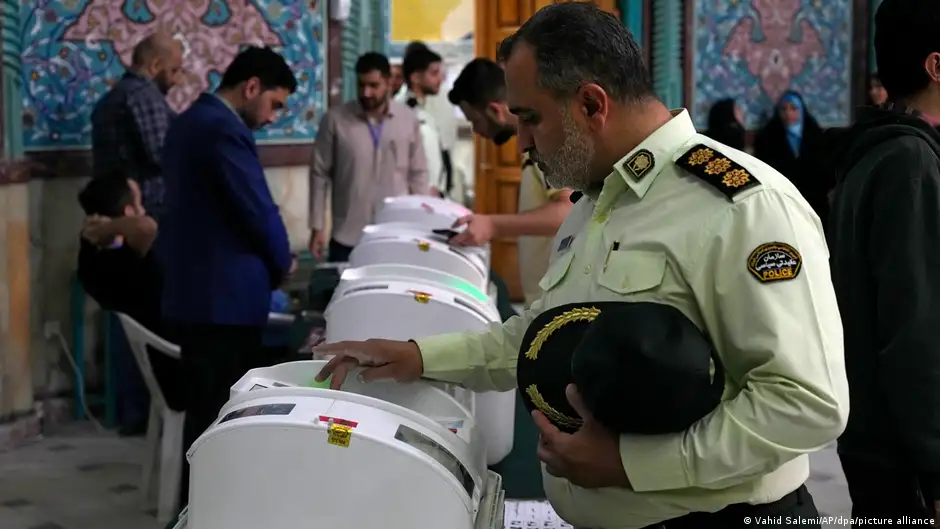 Two men in uniform and a man in a suit enter something in a machine at a polling station in Iran