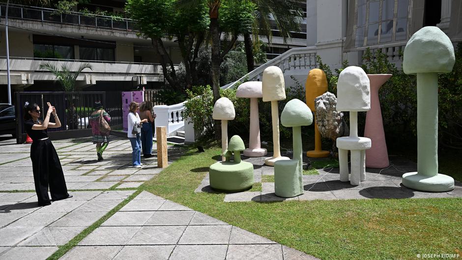A woman uses her smartphon to take a photograph of pastel mushroom-like sculptures outside a building