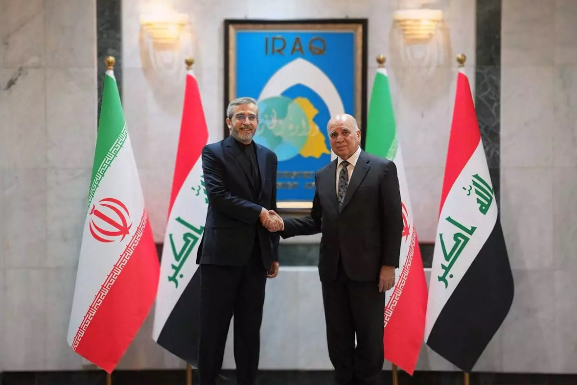 Iranian Foreign Minister Ali Bagheri (left) and Iraqi Foreign Minister Fuad Hussein (right) meet and shake hands in front of national flags in Baghdad, Iraq