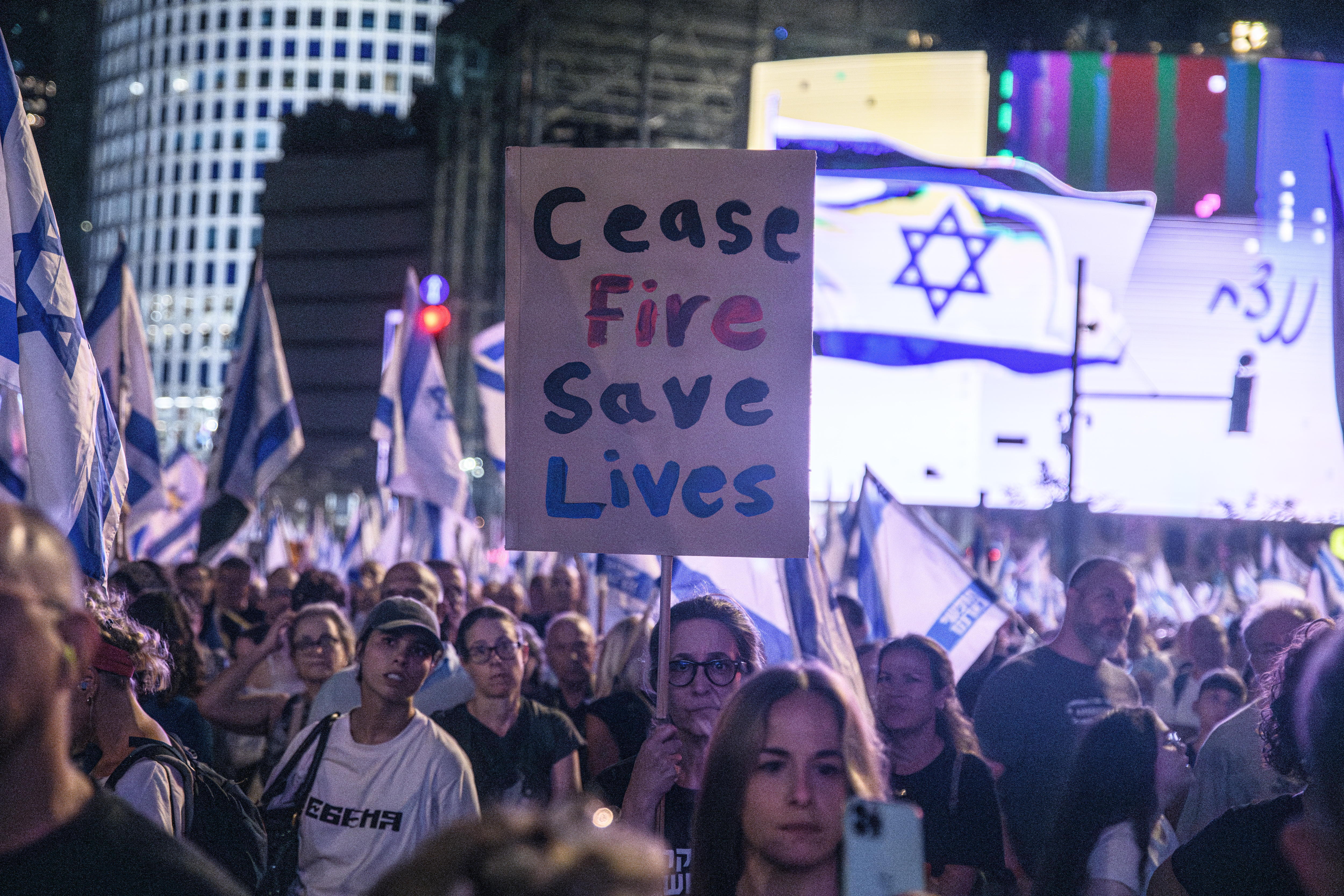 Demonstrierende in Israel. Eine Frau hält ein Schild hoch auf dem "Waffenruhe Rette Leben" steht