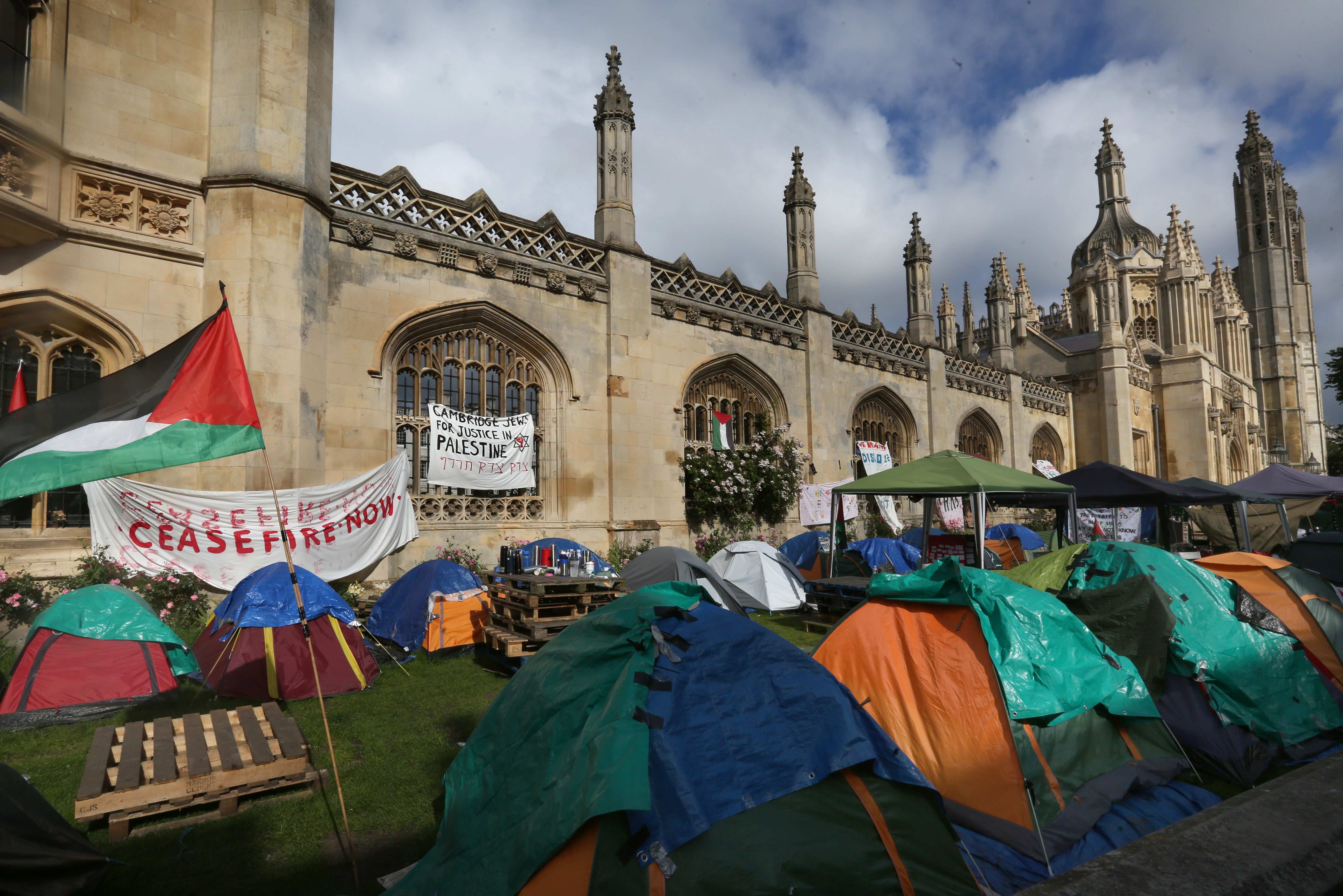 The photo shows a protest camp and placards outside Cambridge University