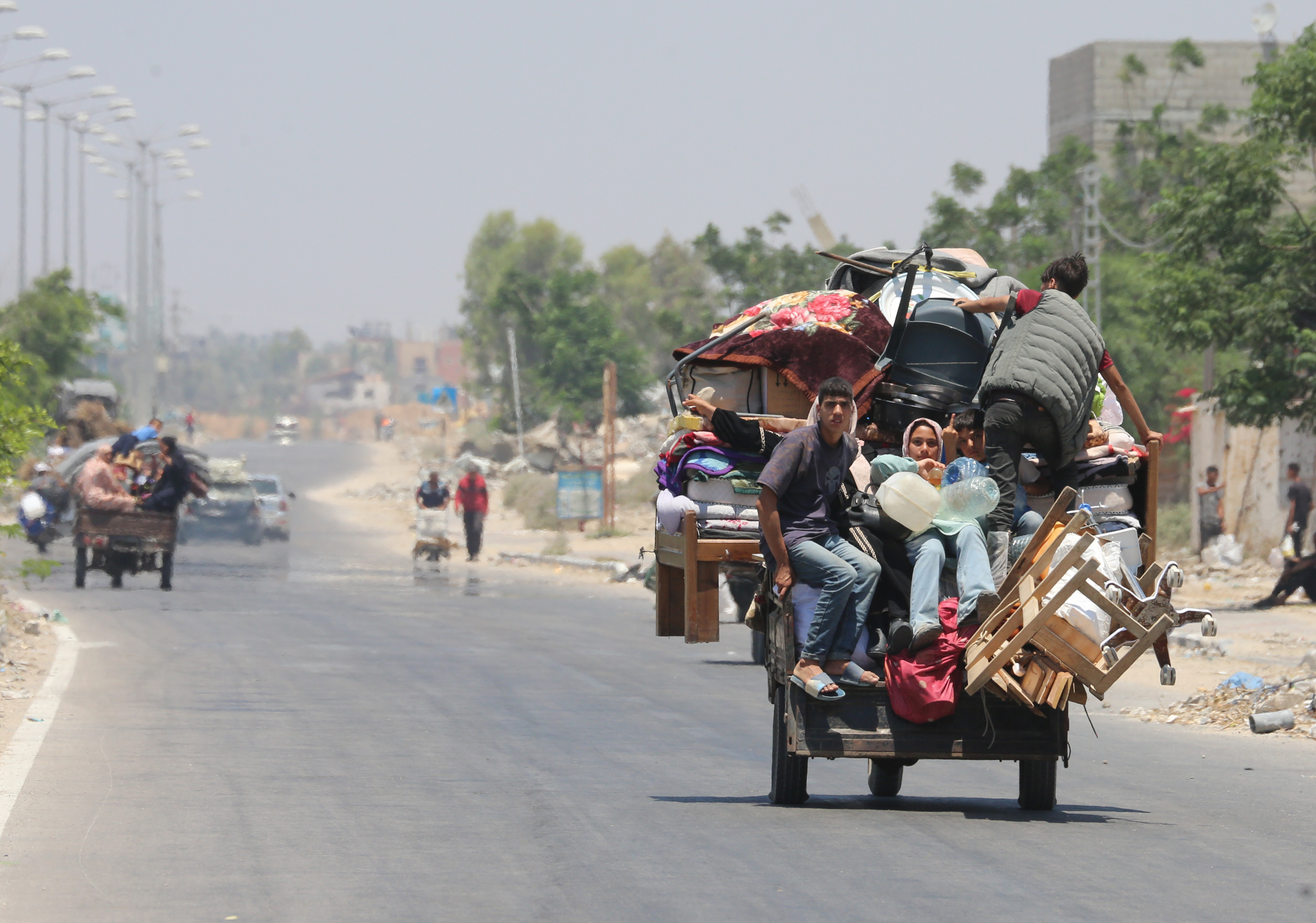 Young people in Gaza sit on a cart loaded with furniture and other belongings and leave the destroyed city