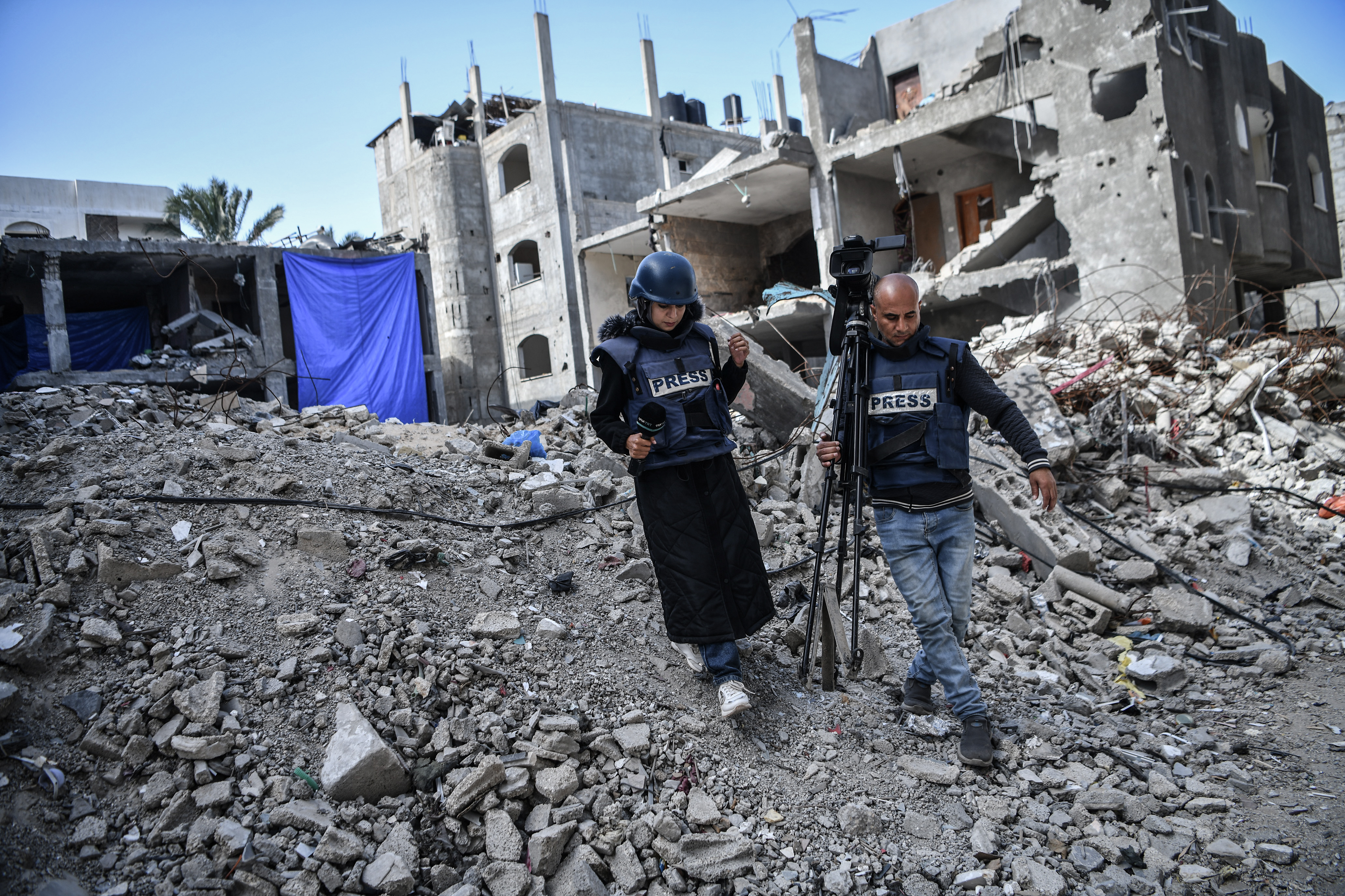 View of destroyed houses in the Gaza Strip. A journalist and a cameraman are walking in the foreground.