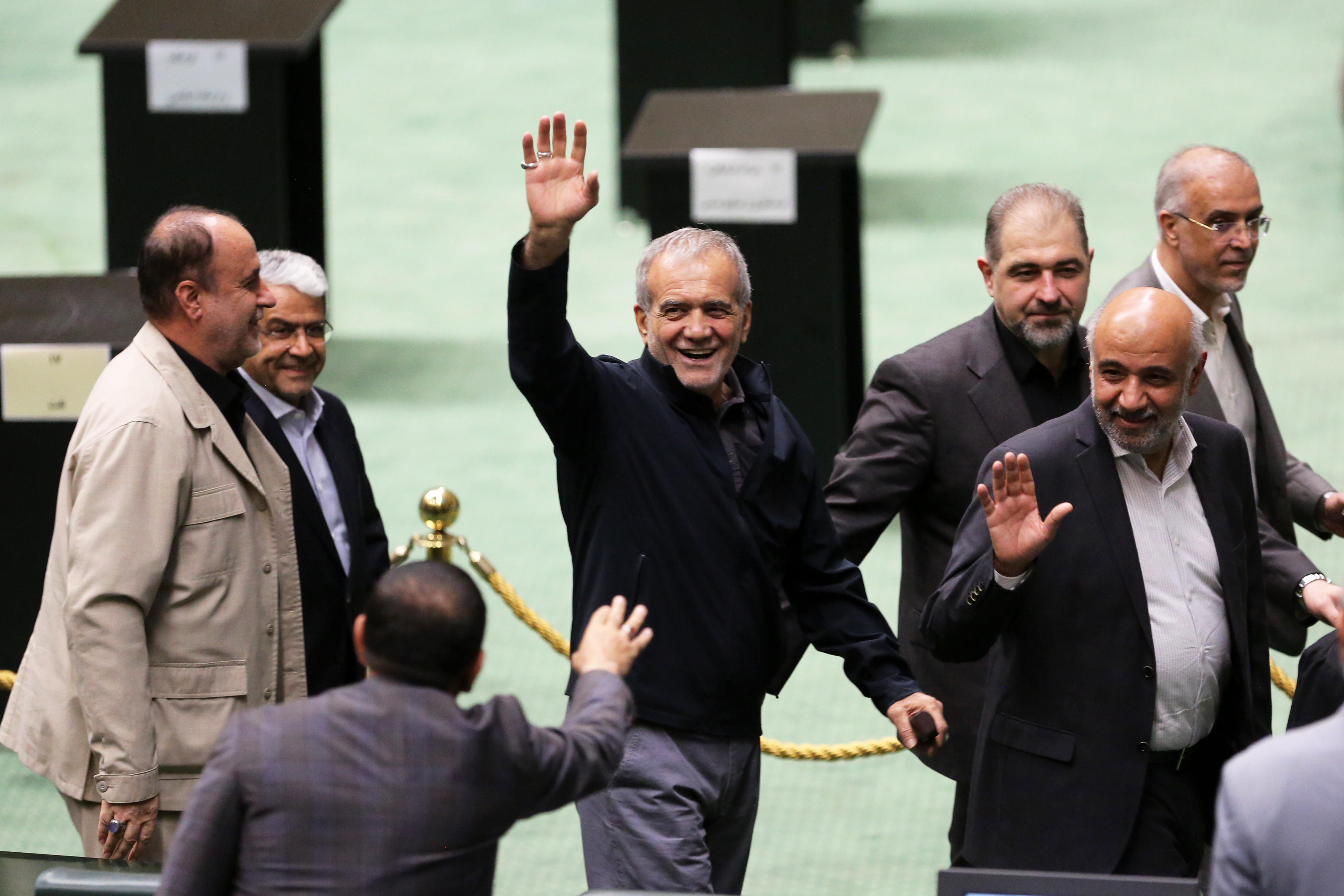 Iran's President Pezeshkian, surrounded by members of the parliament, waving and laughing