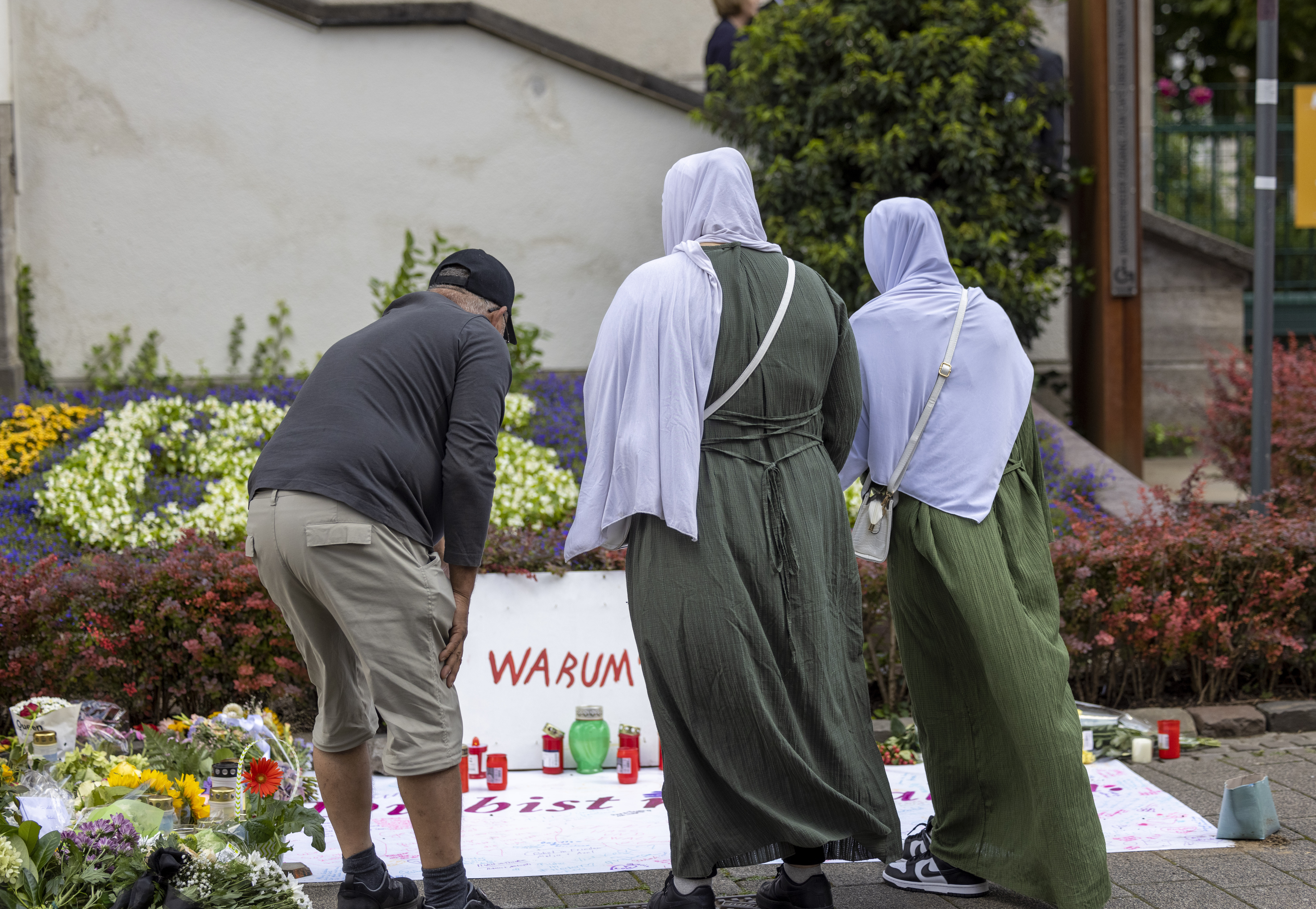 A man and two women wearing headscarves stand in front of a memorial plaque for the victims of the knife attack in Solingen.