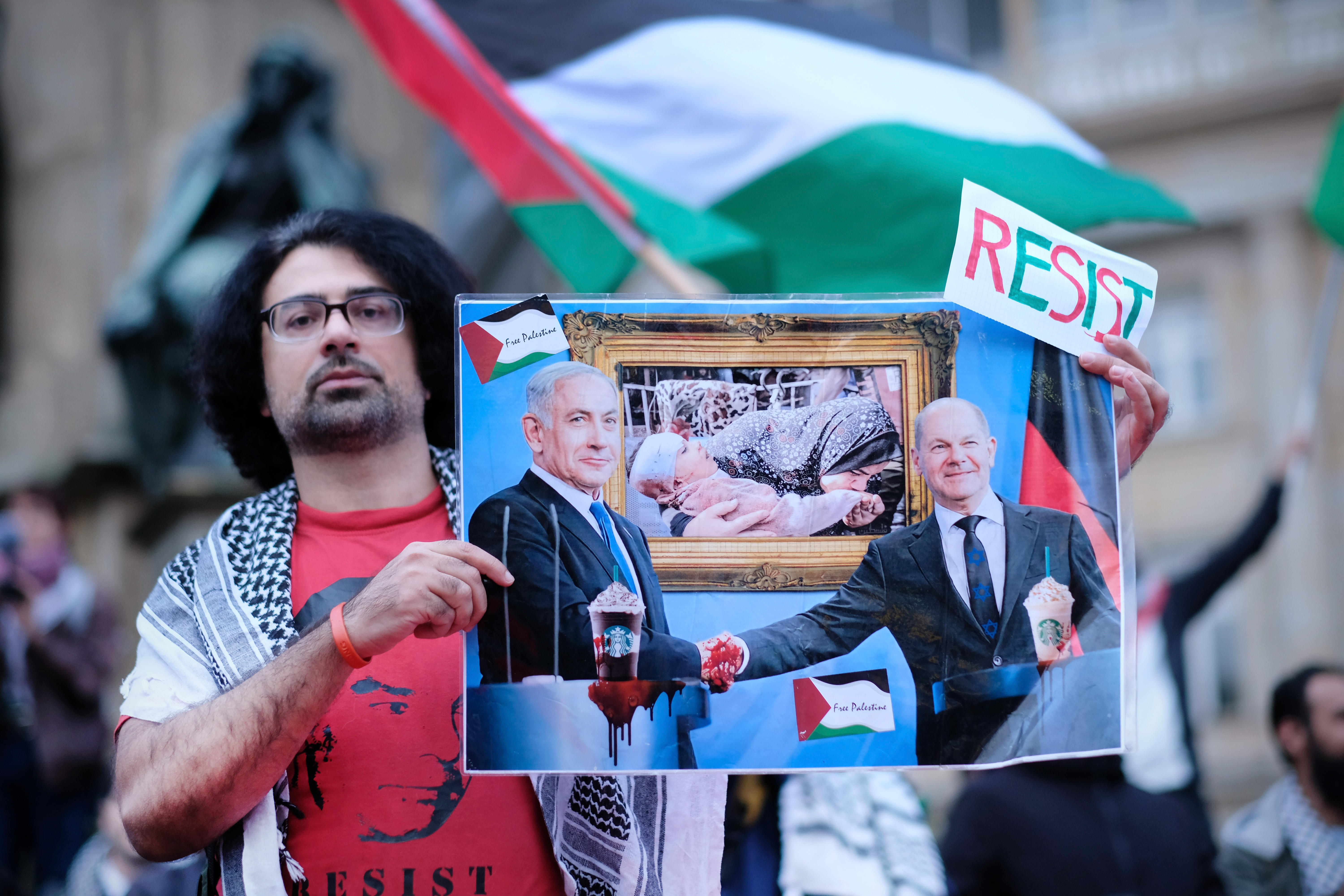 Demonstrant hält eine Karikatur von Netanjahu und Scholz in der Hand