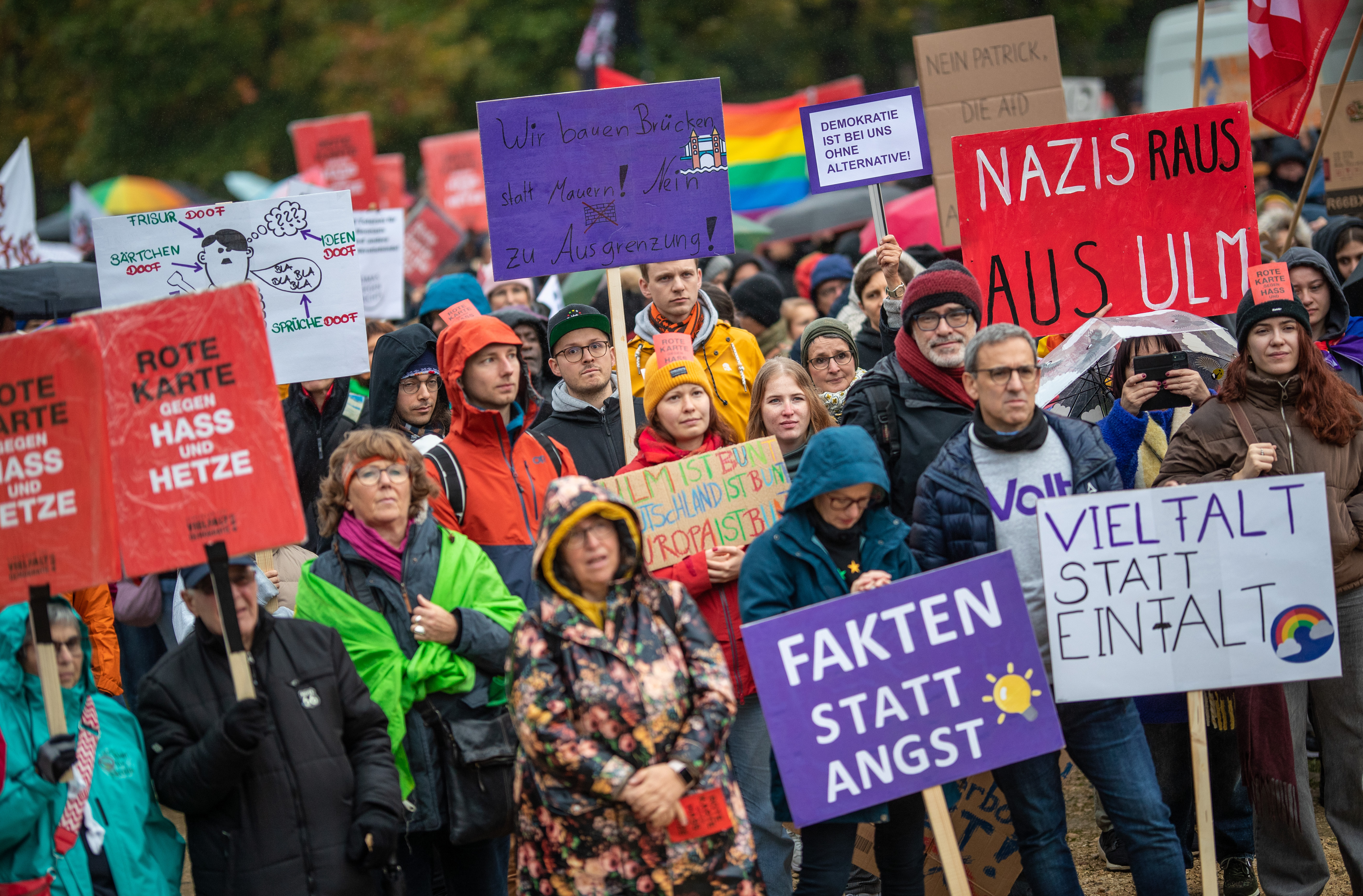 A crowd holding signs and banners demonstrate against the far right.