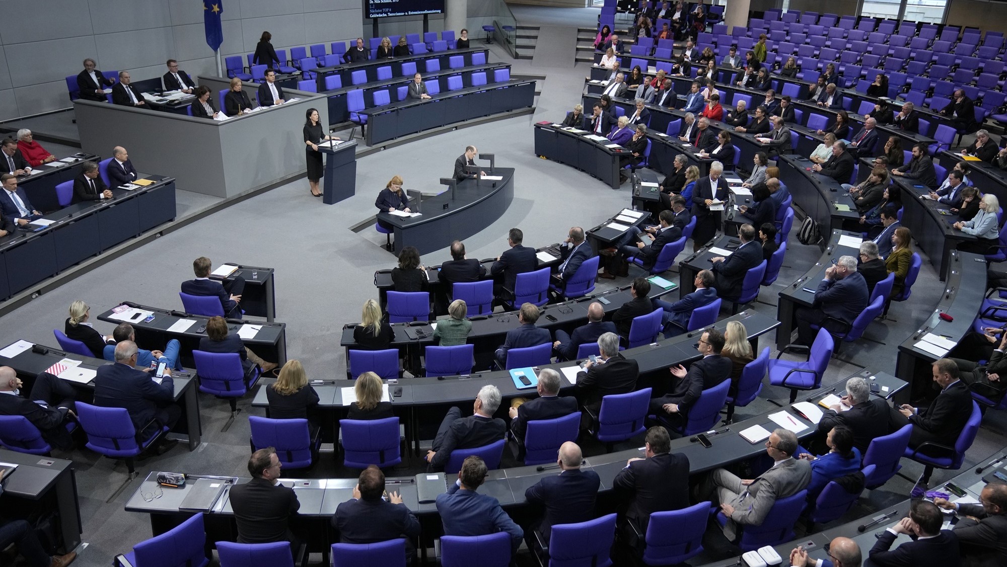 Annalena Baerbock stands at a podium in the centre giving a speech to a crowd of seated people wearing suits.