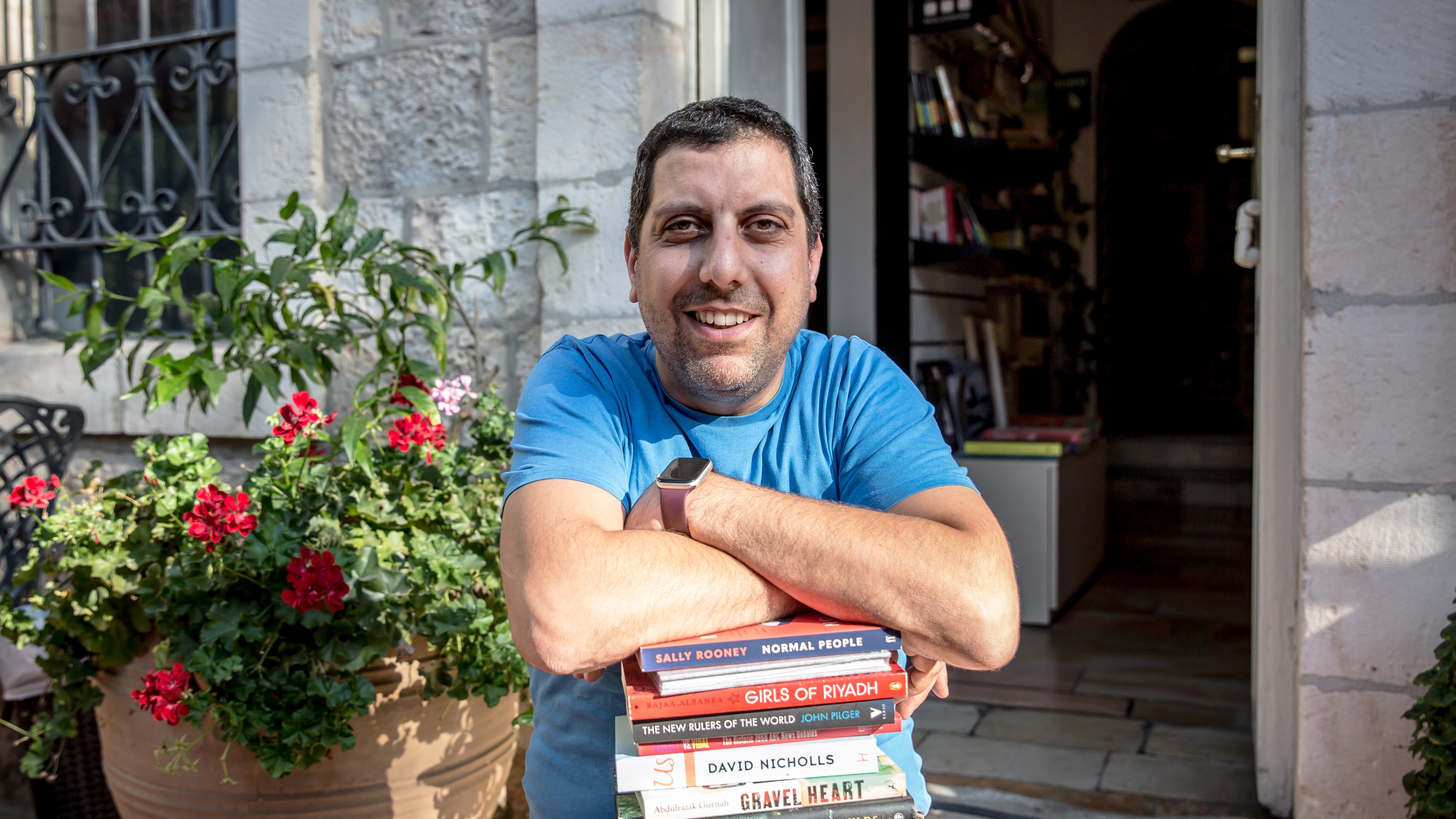 A man leans on a pile of books and smiles into the camera