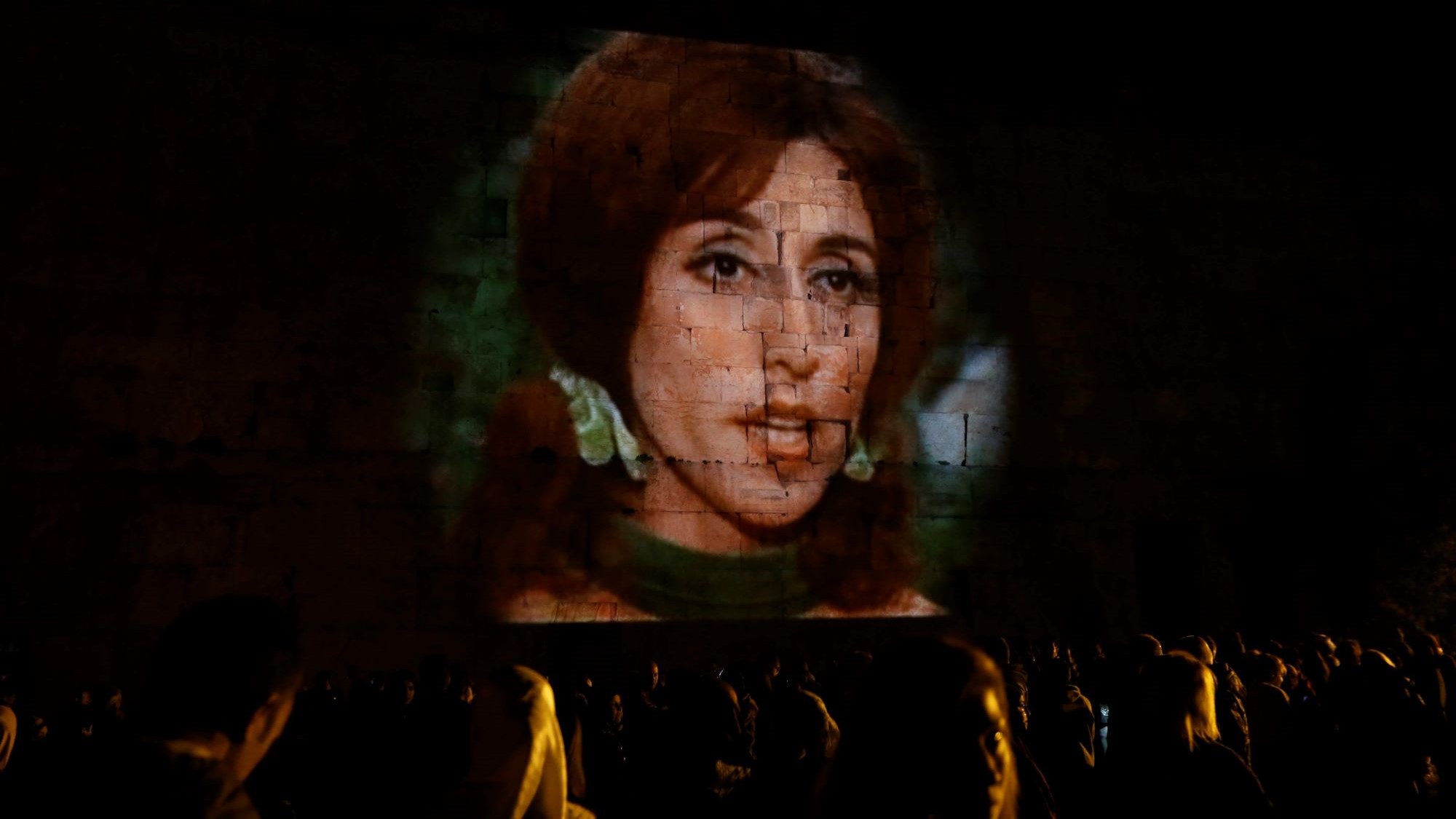 The face of a woman is projected onto a wall made of large stone blocks.