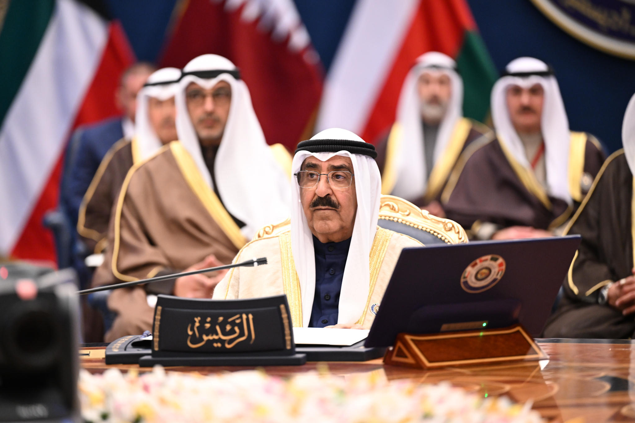 The emir of Kuwait sits at a conference table with a microphone in front of his face.