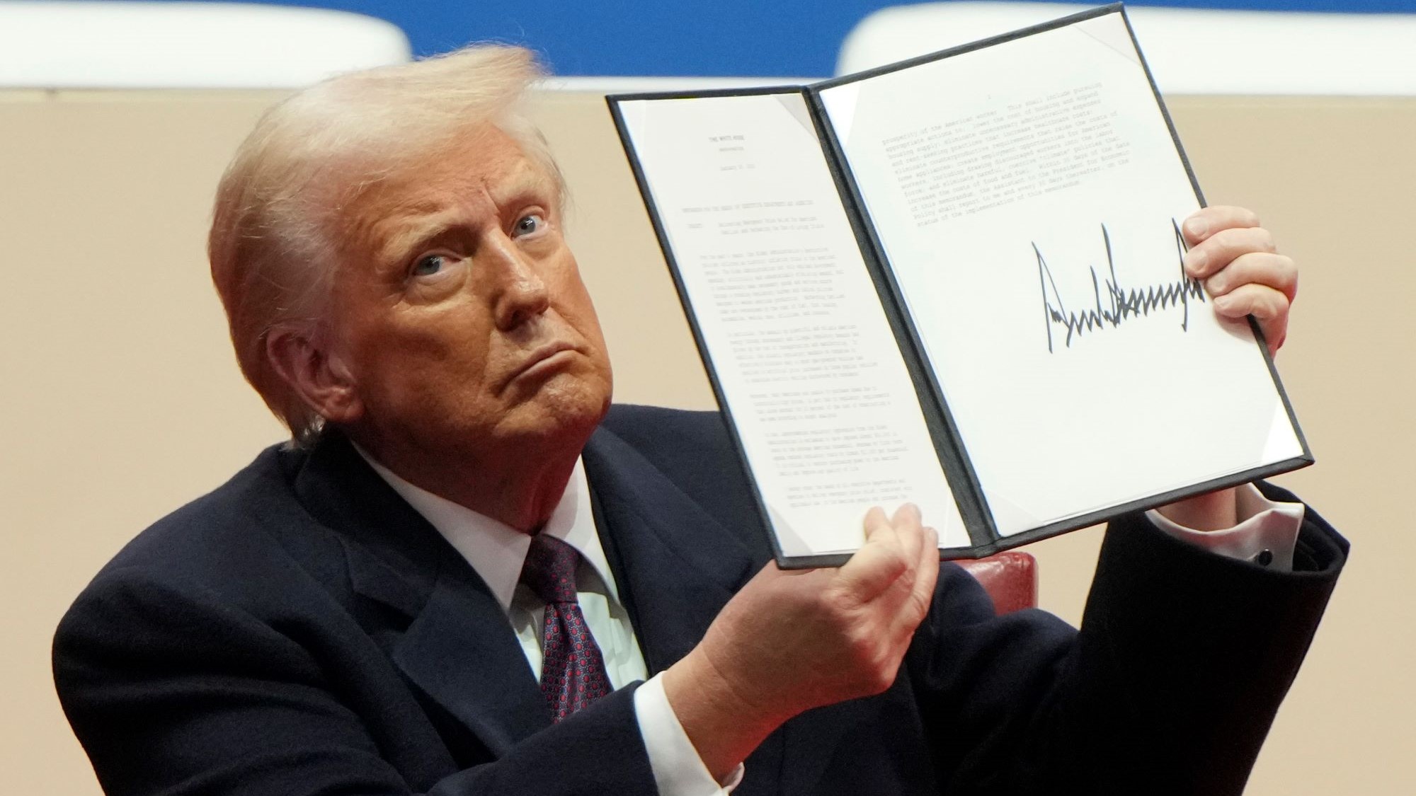 Trump holding  a document to the camera, his signature clearly visible at the bottom.