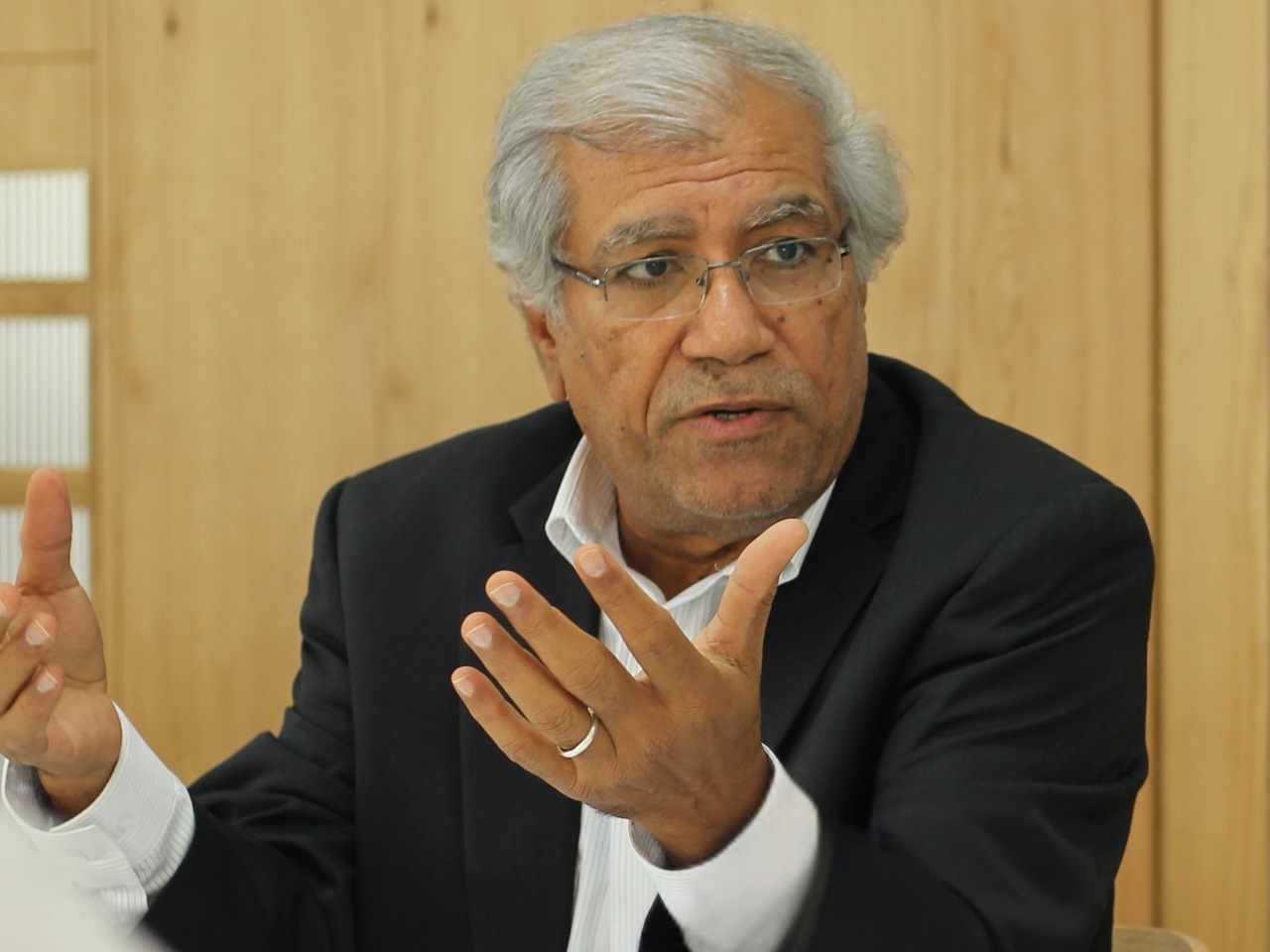 A man raises his hands while speaking. He is wearing a suit.