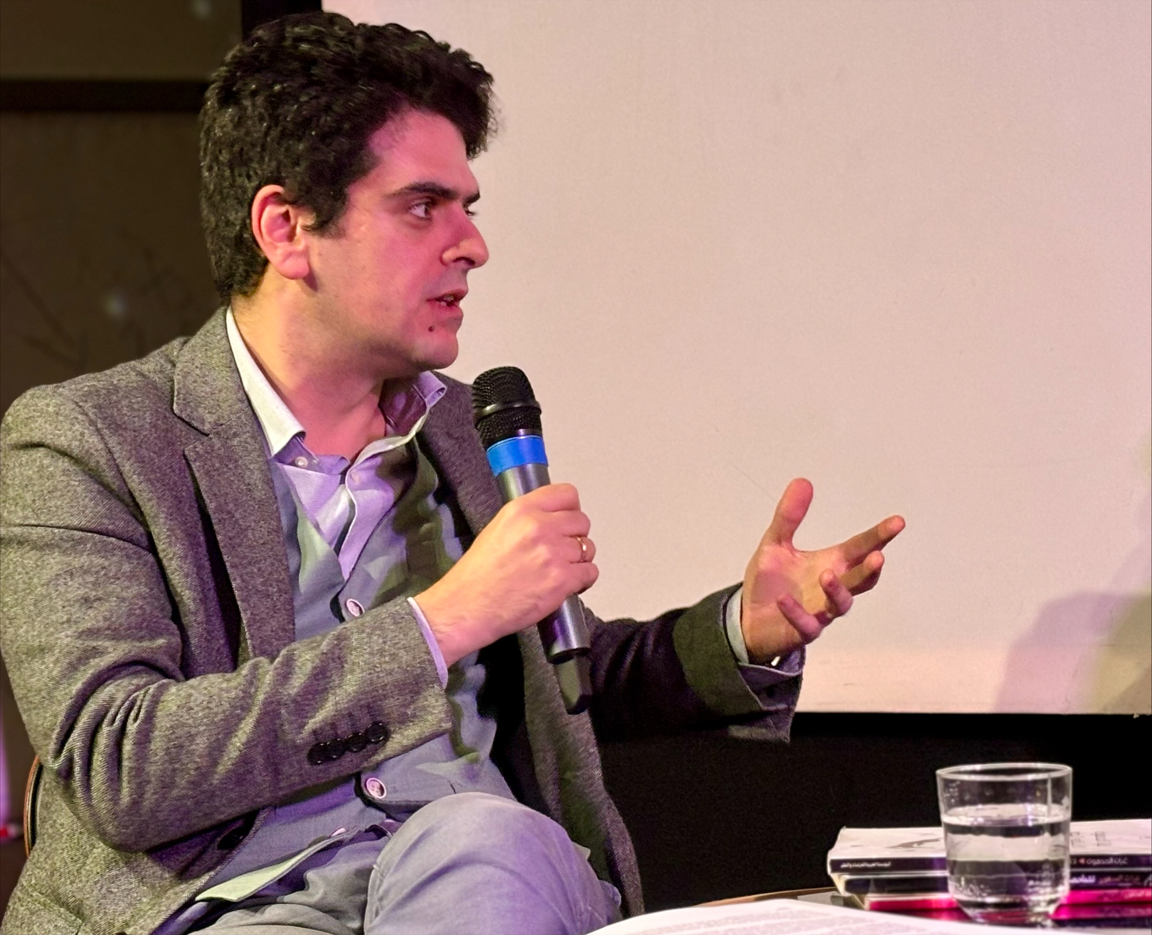 A man sitting in a chair on stage talking into a microphone.