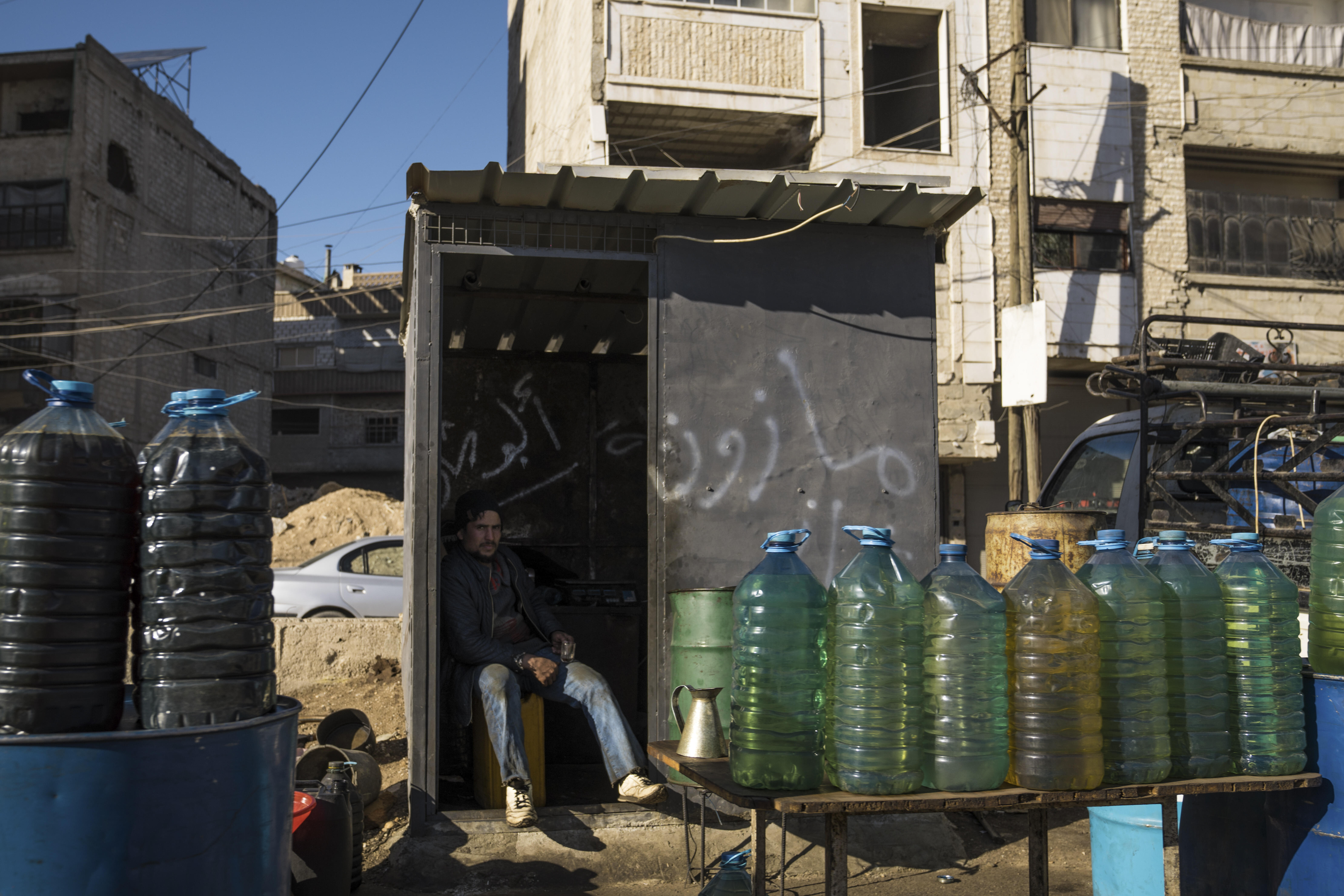 A man sells fuel from plastic bottles on the road in Syria