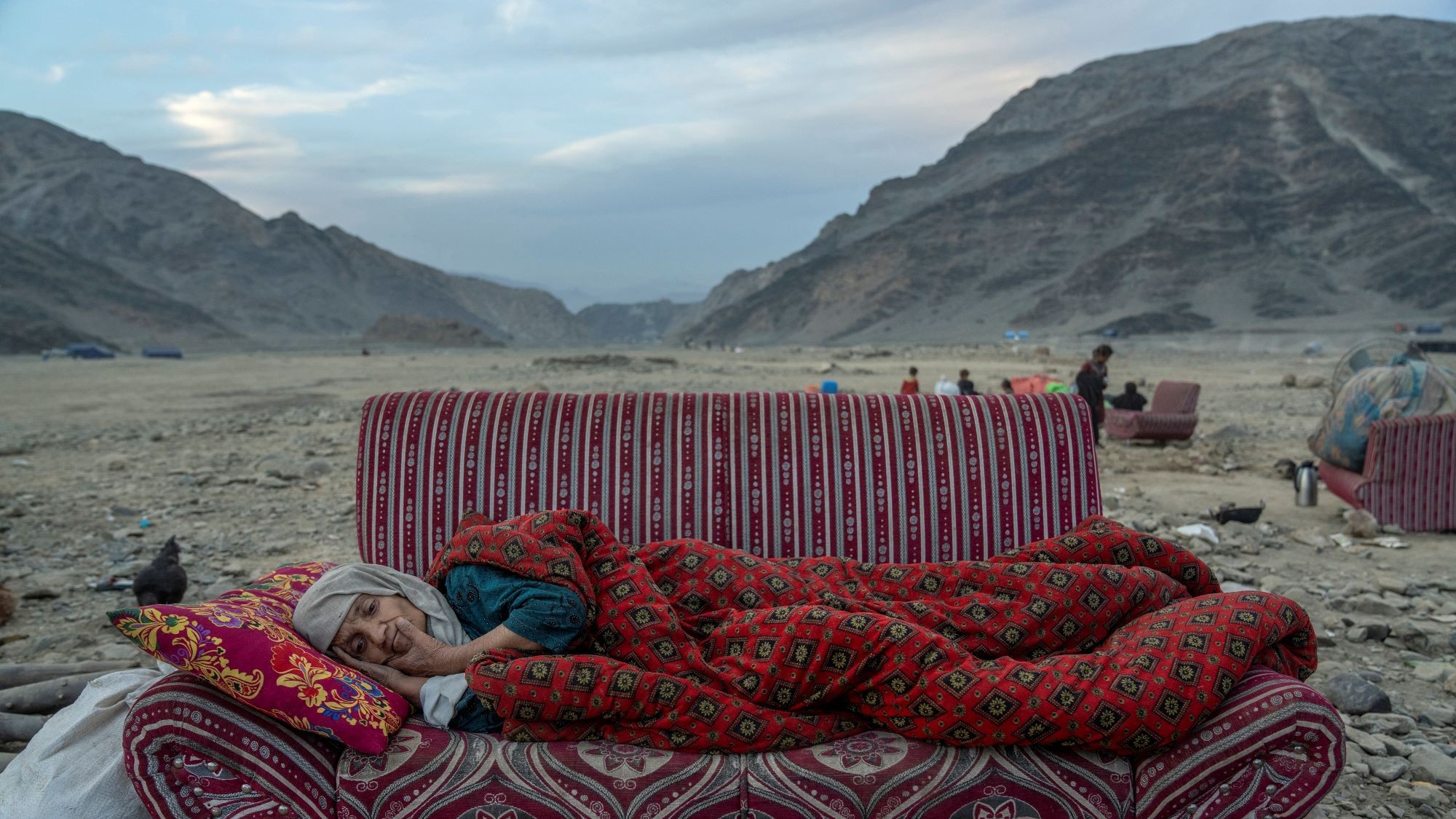 Eine alte Frau liegt auf einem Sofa, das in einer steinigen Landschaft steht.