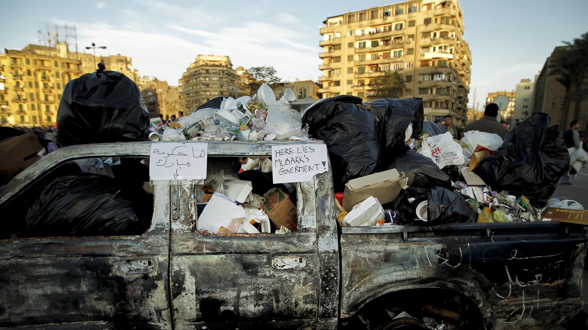 Tahrir Square in Cairo, January 2011. (Photo: picture alliance / AP | T. Todras-Whitehill) A burnt out truck full of trash bags. On the window frame a sign reads "Here lies Mubark's government!"