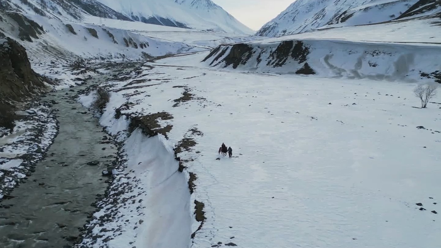 Der beschwerliche Weg über die Berge. Photo: Promo/LittledreamPictures Eine verschneite Gebirgslandschaft, in der Mitte zwei Personen mit Pferd