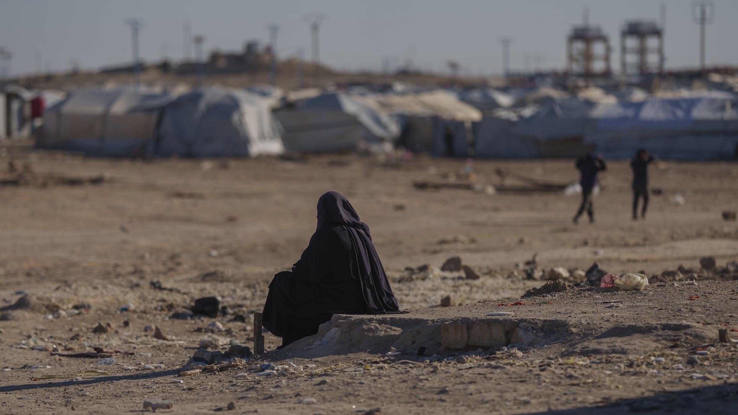Al-Hol camp, Syria. (Photo: picture alliance / AP | B. Armangue) A woman sits in the foreground. In the background tents of a camp are visible.