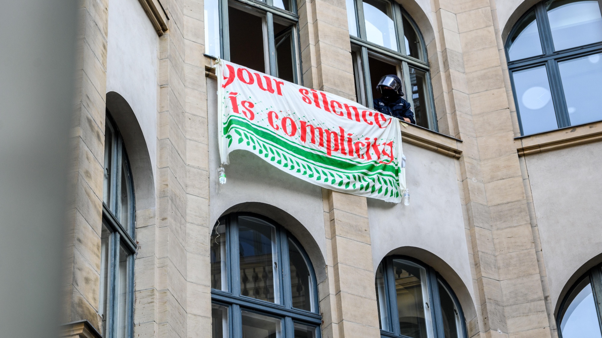Humboldt University, Berlin, 23 May 2024. (Photo: picture alliance / Middle East Images | S. Frank) The facade of a building with a sign hanging from the windows reading "Your silence is complicity"