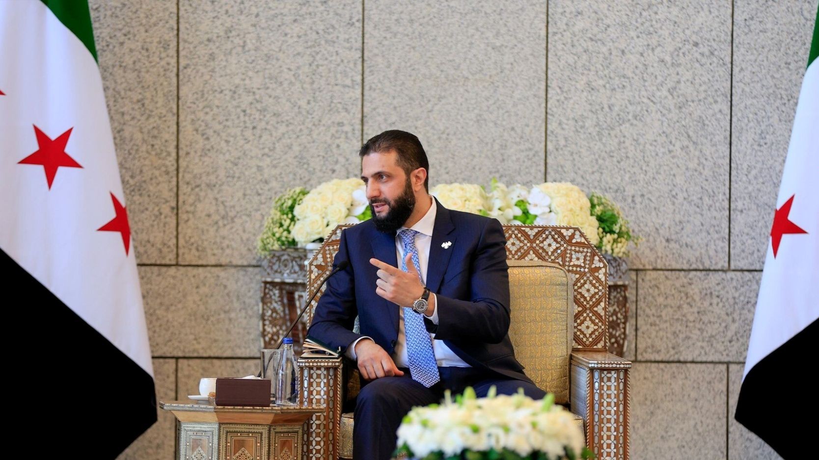 Ahmad al-Sharaa empfängt am 5. Juli 2025 Gäste aus dem Libanon. Foto: Picture Alliance / ZUMAPRESS.com | Syrian Arab News Agency SANA Der syrische Präsident al-Scharaa sitzt zwischen zwei syrischen Flaggen auf einem prachtvollen Stuhl.