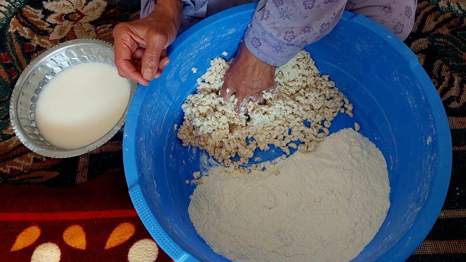 أم فلسطينية تخبز ما توفر من طحين داخل منزلها في مخيم النصيرات، 19 يونيو/حزيران 2025. (Photo: Copyrights for Qantara/Doaa Shahin) امرأة تقوم بخلط الدقيق بالمعكرونة.