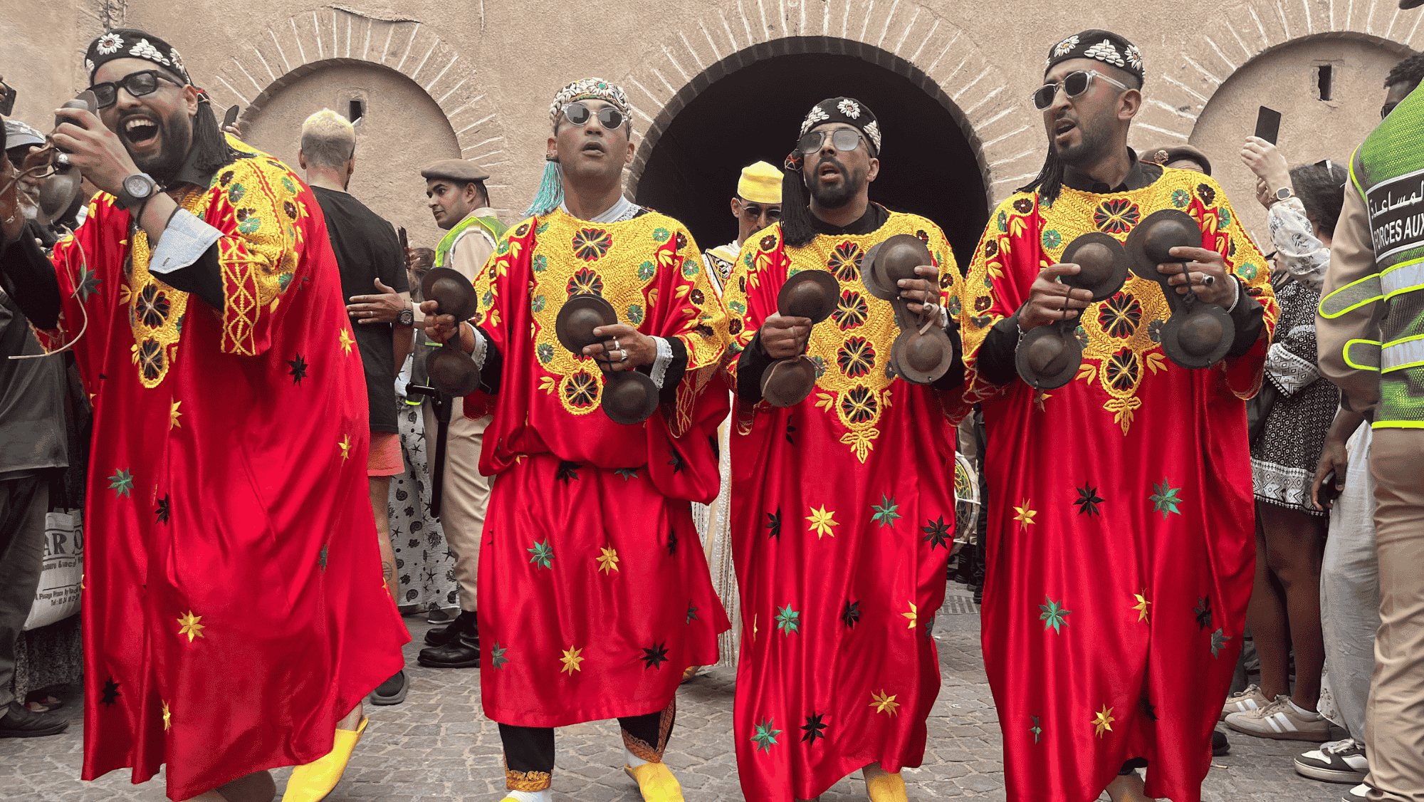 Vier Gnaoua-Musiker laufen durch Essaouira mit Kastagnetten und in roten Gewändern, die mit gelben und grünen Stickereien verziert sind.