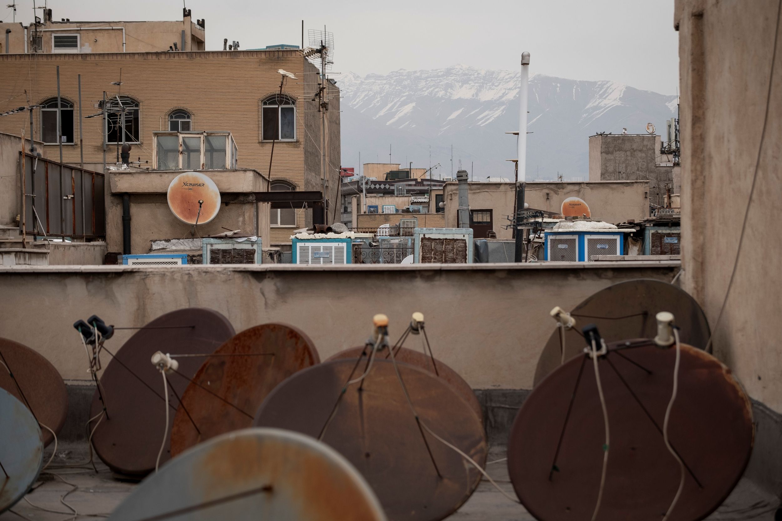 Satellite dishes on a rooftop, other buildings and mountains in the distance.