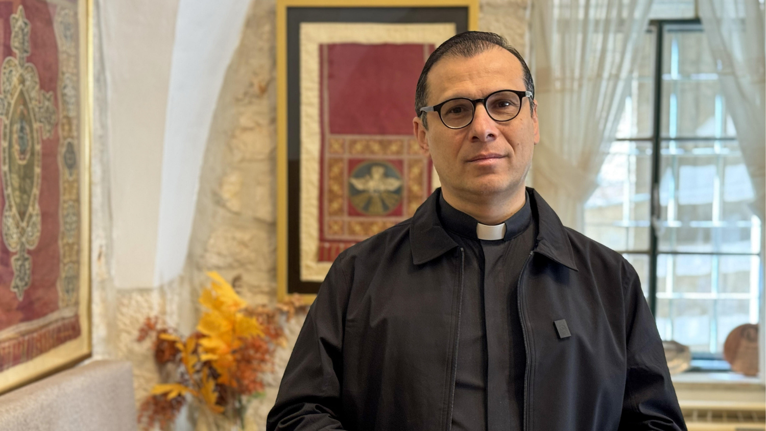 Munther Isaac (Foto: picture alliance/Anadolu | Hisham K. K. Abu Shaqra) Munther Isaac steht im Pastor-Gewand in einem Raum der Evangelisch-Lutherischen Kirche in Bethlehem